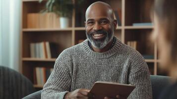 MiddleAged Man of African Descent Smiling, Holding a Tablet in Cozy Library Setting, Perfect for Professional Use in Articles, Blogs, and Social Media Campaigns photo