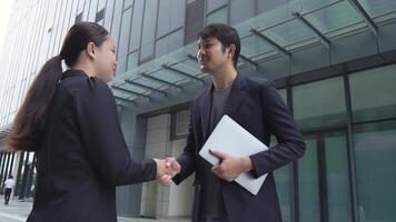 Asian businessman and woman shaking hands behind office building, business collaboration concept and connection for success. video
