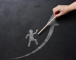 A hand draws a picture of a person walking on an upward arrow on a blackboard with chalk, symbolizing personal growth, success and progress. Concept of development and goal achievement photo