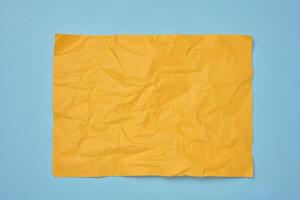 Crumpled rectangular sheet of yellow paper on a blue background, top view. Place for inscription photo