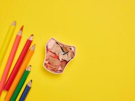 Multicolored wooden pencils and sharpener on yellow background, top view photo