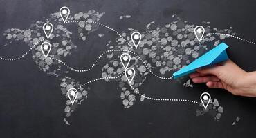 Hand holding blue paper airplane against world map background with dotted lines connecting different locations, global travel or logistics concept photo