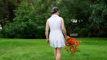 a woman in a white dress is walking through a field with a bunch of red lantern plants video