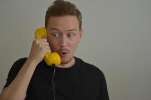 A man talking on the phone with a yellow retro telephone receiver. Emotion expression of surprise astonishment concept. Emotional reaction from the conversation. Banner background with copy space photo