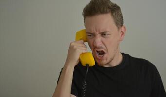 A man talking and shouting on the phone with a yellow retro telephone receiver. Emotion expression of anger concept. Emotional reaction from the conversation. Banner background with copy space photo