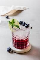 Blueberry mojito with ice, lemon and mint in a glass on marble photo