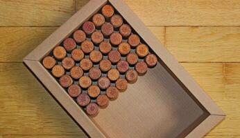 A box filled halfway with wine corks at an angle on wooden planks surface top view photo