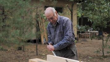 An experienced craftsman is focused on chiseling a wooden part with a chisel and hammer. The serene surroundings highlight his dedication to traditional woodworking. video
