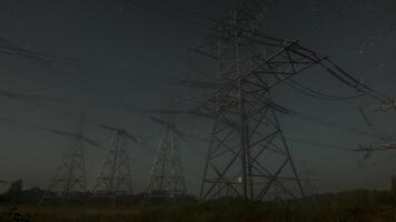 Nighttime view of high voltage power lines against the backdrop of moving stars in the night sky on a moonlit night. Concept of electricity and energy generation video