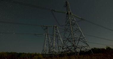 Nighttime view of high voltage power lines against the backdrop of moving stars in the night sky on a moonlit night. Concept of electricity and energy generation video