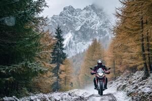 Motorcyclist riding adventure motorcycle on snowy forest path in the italian dolomites photo