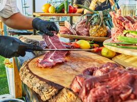 A close-up view of a chefs gloved hand holding raw beef cuts, preparing them on a wooden board, showcasing texture and marbling photo