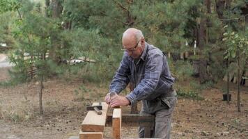 A craftsman meticulously shapes a wooden plank using hand tools in an outdoor workspace, surrounded by nature, showcasing skillful woodworking techniques. video