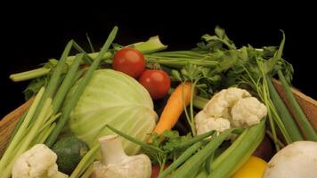 A wooden crate filled with fresh vegetables. The crate contains a variety of colorful produce, including tomatoes, green peppers, yellow peppers, cabbage, cucumbers, scallions, and corn. video