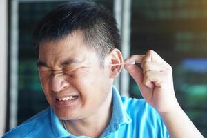 Asian man make face expression during using cotton bud stick to remove earwax. Concept, Health care. Use cotton swab in ear can hurt ear drums and hearing loss. Ear cleaning photo