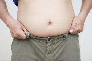 Close up man tries to pull up his trousers for wearing with big belly. Concept, fat, overweight, health problem of obesity, overweight in men can cause to diseases. photo