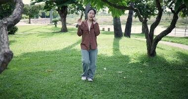 Handheld shot, Happy woman enjoys talking on her mobile phone while walking in a park. A holiday time surrounded by nature video