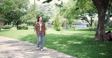 Handheld shot, Happy young woman enjoys a leisurely stroll, immersing herself in the nature around her in a park, enjoying the sunlight filtering through the trees along the way. video