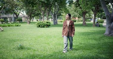 Handheld shot, Happy young woman enjoys a leisurely stroll, immersing herself in the nature around her in a park, enjoying the sunlight filtering through the trees along the way. video