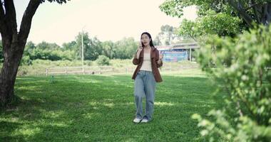 Handheld shot, Happy woman enjoys talking on her mobile phone while walking in a park. A holiday time surrounded by nature video