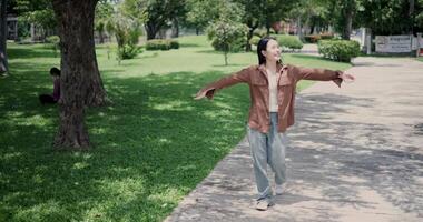 Handheld shot, Happy young woman enjoys a leisurely stroll, immersing herself in the nature around her in a park, enjoying the sunlight filtering through the trees along the way. video