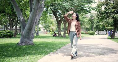 Handheld shot, Happy young woman enjoys a leisurely stroll, immersing herself in the nature around her in a park, enjoying the sunlight filtering through the trees along the way. video