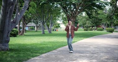 Handheld shot, Happy woman enjoys talking on her mobile phone while walking in a park. A holiday time surrounded by nature video