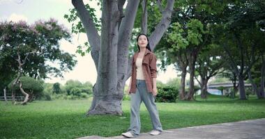 Handheld shot, Happy young woman enjoys a leisurely stroll, immersing herself in the nature around her in a park, enjoying the sunlight filtering through the trees along the way. video
