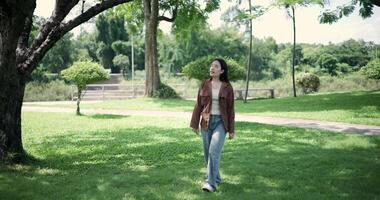 Handheld shot, Happy young woman enjoys a leisurely stroll, immersing herself in the nature around her in a park, enjoying the sunlight filtering through the trees along the way. video