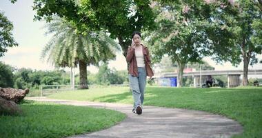 Handheld shot, Happy woman enjoys talking on her mobile phone while walking in a park. A holiday time surrounded by nature video