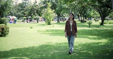 Handheld shot, Happy young woman enjoys a leisurely stroll, immersing herself in the nature around her in a park, enjoying the sunlight filtering through the trees along the way. video