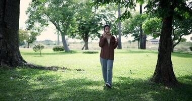 Handheld shot, Happy woman enjoys talking on her mobile phone while walking in a park. A holiday time surrounded by nature video