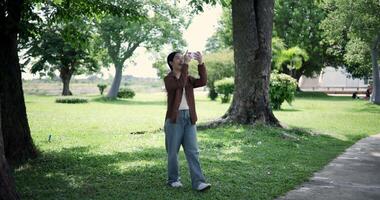 Handheld shot, Happy woman enjoys takes a photo on mobile phone while walking in a park. A holiday time surrounded by nature video
