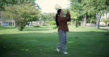 Handheld shot, Happy woman enjoys takes a photo on mobile phone while walking in a park. A holiday time surrounded by nature video