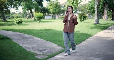 Handheld shot, Happy woman enjoys talking on her mobile phone while walking in a park. A holiday time surrounded by nature video