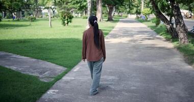 Handheld back view shot, Relaxed woman is enjoying a leisurely stroll and looking around a park filled with fresh air and soft sunlight. Enjoy a happy holiday video