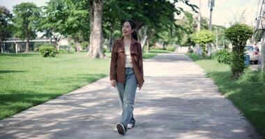Handheld shot, Happy young woman enjoys a leisurely stroll, immersing herself in the nature around her in a park, enjoying the sunlight filtering through the trees along the way. video