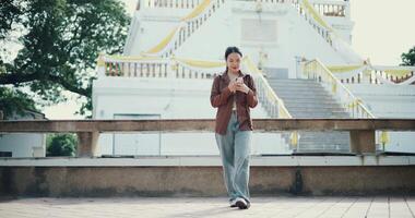 Handheld low angle view shot, Relaxed woman enjoying social media or chatting on mobile phone while walking in public park ,Holiday leisure activities video