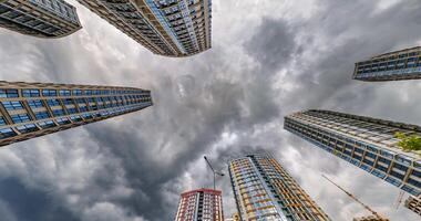 loop circular motion and view up from ground to storm clouds sky among skyscrapers, look at house from bottom up video