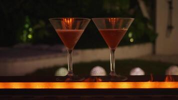 Fireside two glasses of alcohol on bar with fire glow adding touch of warmth and luxury to drinking experience. Elegant evenings flames in background two glasses of alcohol on bar night of enjoyment. video