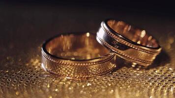 Wedding rings lying, rotate, spinning on shiny golden shining surface with light, close-up macro video