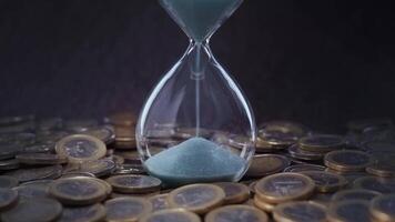 Sand flows into hourglass with coins around video