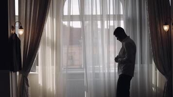 Man in jacket fastens buttons, buttoning white shirt preparing to go out, walking near window video
