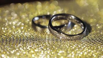 Wedding rings lying, rotate, spinning on shiny golden shining surface with light, close-up macro video