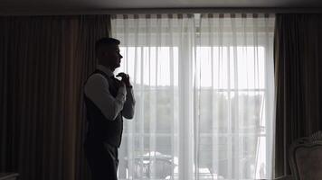 Man in jacket fastens buttons, buttoning white shirt preparing to go out, walking near window video