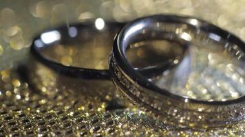 Wedding rings lying, rotate, spinning on shiny golden shining surface with light, close-up macro video