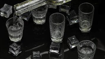 Barman pour frozen vodka from bottle into shot glass. Ice cubes against dark wet black background video
