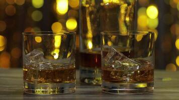 Barman pushes, puts glass with golden whiskey, cognac or brandy with ice cubes on wooden table video