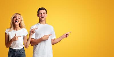 Joyful young guy and girl pointing away at copy space on yellow background photo