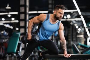 Millennial muscular man working out in gym, doing exercises with dumbbells at biceps, free space photo